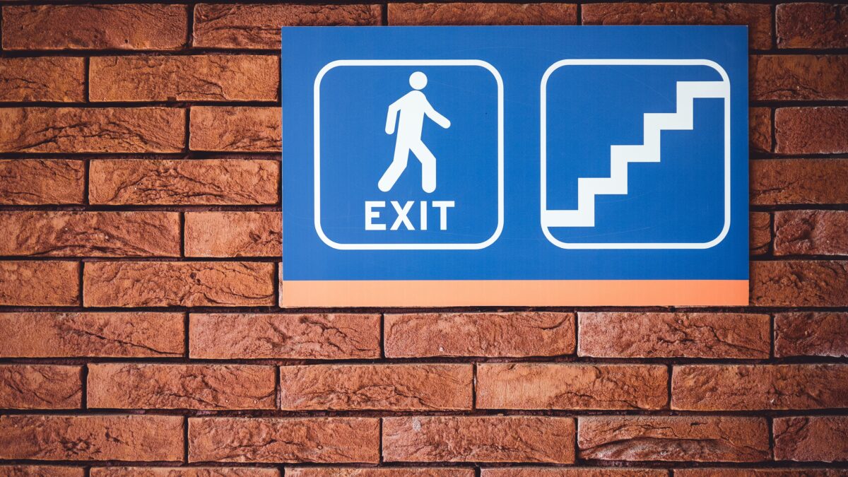 blue and white exit signage mounted on brown brick wall