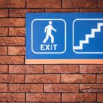 blue and white exit signage mounted on brown brick wall