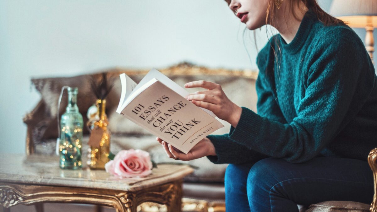 woman sitting down near table reading 101 Essays book